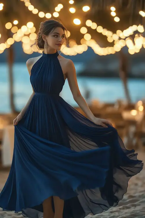 A mature woman in a navy blue sleeveless chiffon gown with a flowing skirt and cinched waist, accessorized with pearl earrings and gold wedge heels