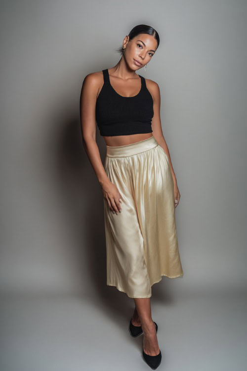 A mid-size woman wearing a silky midi skirt with a cropped knit tank and heeled mules, styled for an effortlessly elegant summer evening, simple studio background