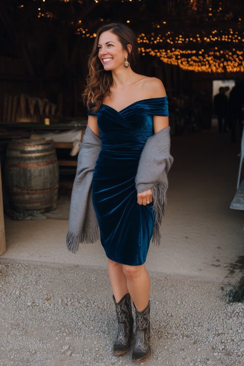 A woman over 40 in a dark teal velvet midi dress with a ruched bodice and off-the-shoulder neckline, styled with embellished cowboy boots and a gray cashmere shawl