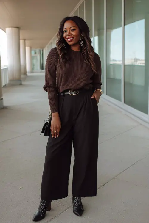 A curvy woman wears a fitted chocolate-brown sweater with black wide-leg trousers and black cowboy boots