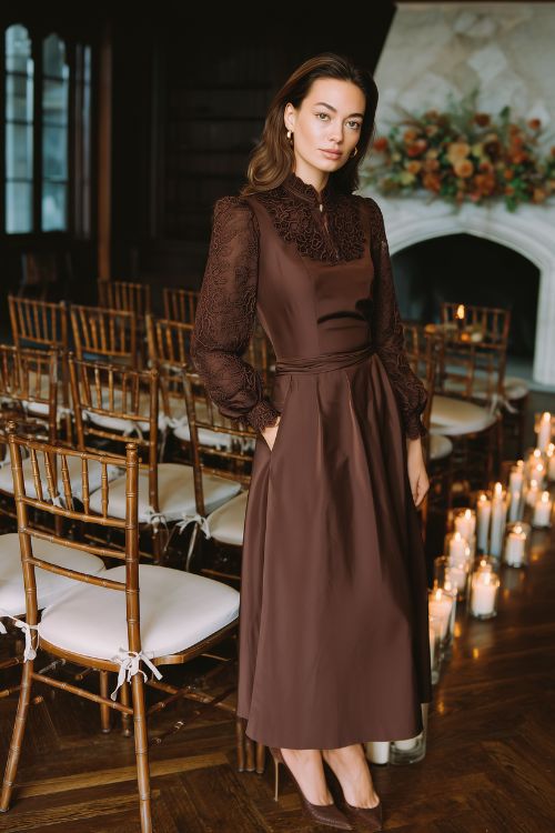 A woman wears a chocolate brown A-line dress with lace sleeves and a defined waistline