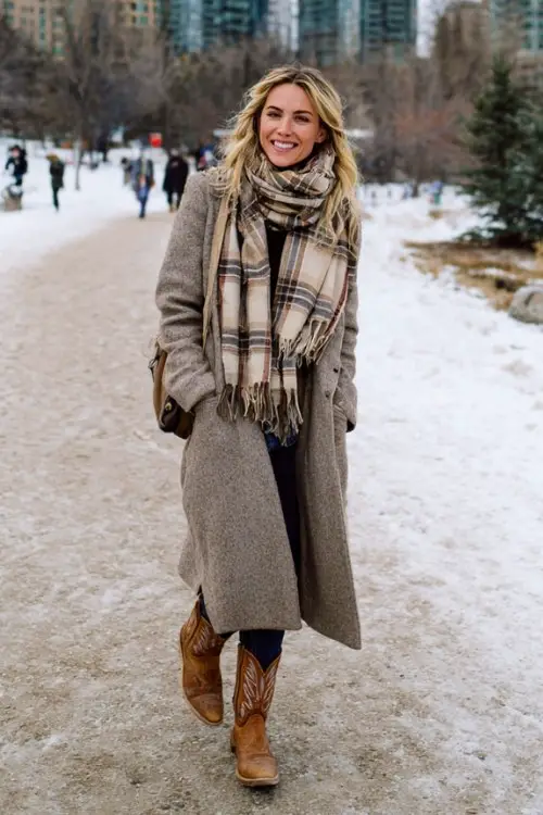 A woman wears a long wool coat, plaid scarf, and cowboy boots