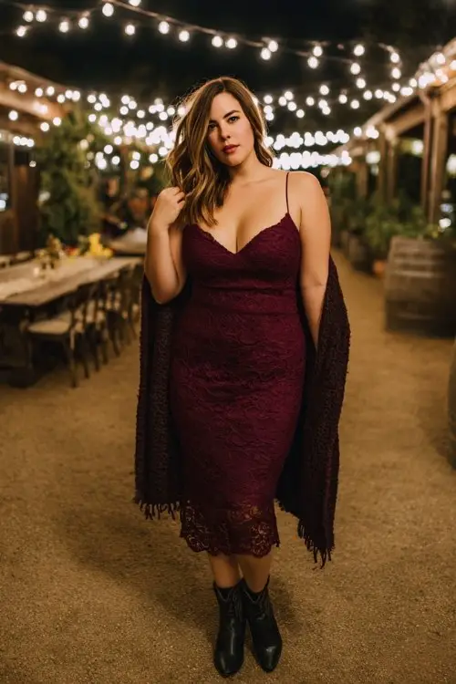 A curvy woman wears a deep burgundy lace midi dress with black cowboy boots