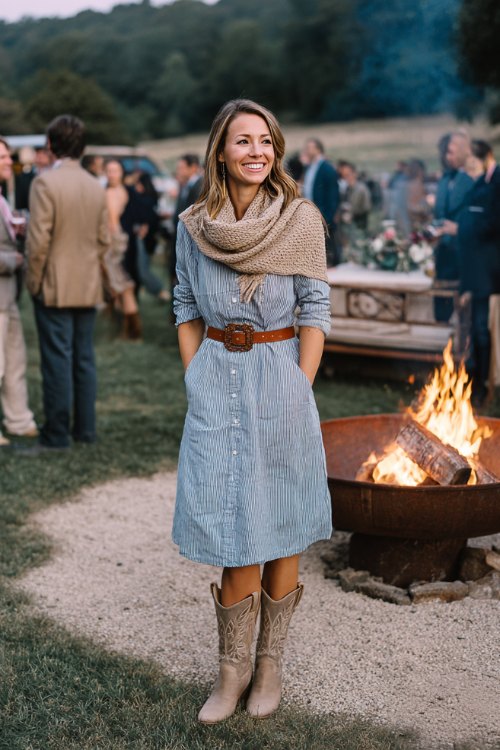 A woman in a chambray shirt dress cinched with a brown leather belt, paired with light suede cowboy boots