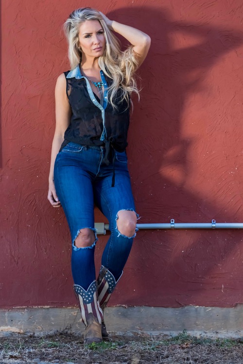 A woman wears cowboy boots with a ripped jeans and a vest