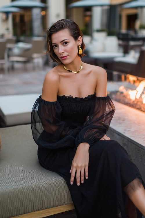 A woman wears a black off-the-shoulder midi dress with sheer sleeves and gold jewelry