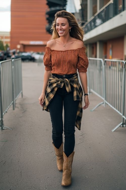 a woman wears an off shoulder rust top with black jeans and tan cowboy boots for fall concert