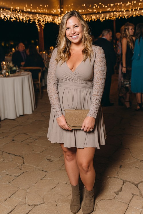 A plus-size woman wears a taupe long-sleeve fit-and-flare dress with delicate lace detailing, paired with ankle boots and a leather clutch